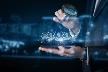 A businessman using a magnifying glass to inspect digital profile icons hovering over a smartphone. 