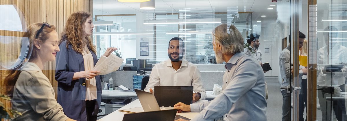 Group of professionals having a meeting in a modern office, with laptops and documents on the table, behind glass walls